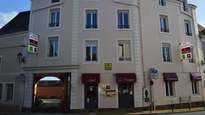 Een meerhoog hotel in klassieke Europese stijl, met een centrale ingang, meerdere ramen en borden die voorzieningen aangeven zoals een restaurant en parkeergelegenheid.