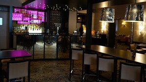 Eine Bar mit einer Theke, Stühlen und Tischen. Auf der Theke stehen Flaschen und Gläser.