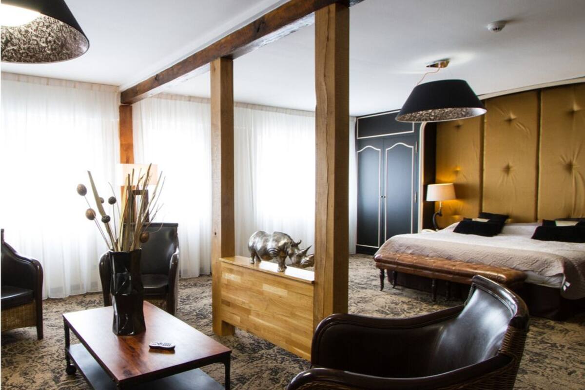 A hotel room with a bed, a wooden dresser, a wicker chair, a coffee table, and a desk.