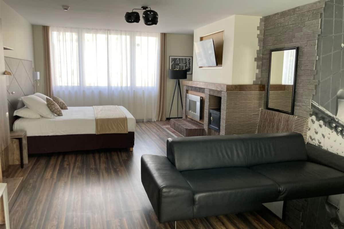 A modern hotel room with a bed, a sofa, a fireplace, and a TV.