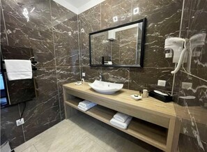 A modern bathroom with a marble wall, a large mirror, a sink, a towel rack, and a hairdryer. - Le Mouton Blanc (Cambrai)