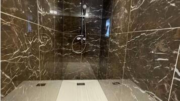 Un baño moderno con paredes y suelo de mármol, cabina de ducha de cristal y ducha visible.