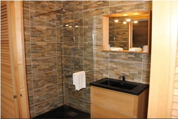 Un baño con ducha de vidrio, tocador de madera con lavamanos negro y un espejo sobre el tocador.