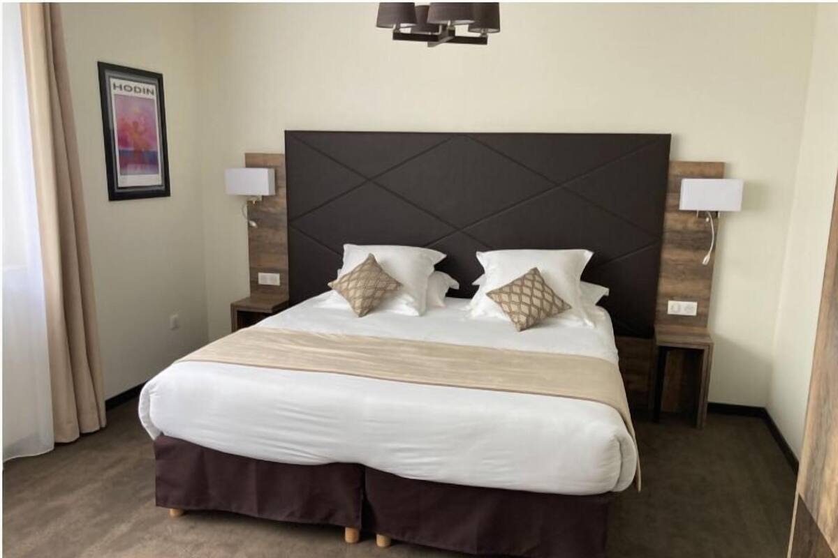 A hotel room with a large bed, two bedside lamps, a framed picture on the wall, and a modern headboard.