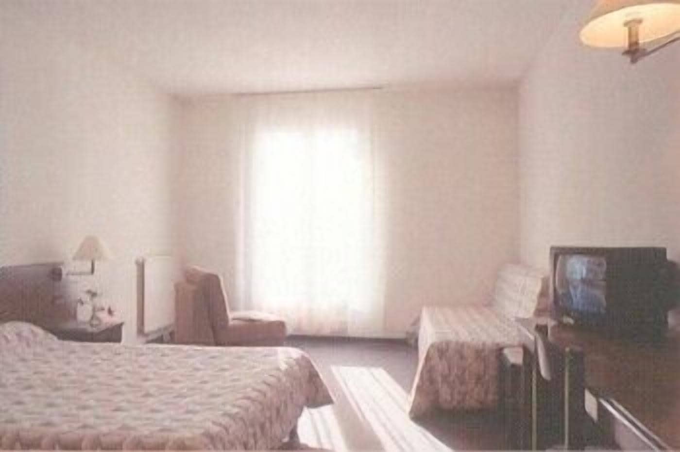 A hotel room with two beds, a desk with a television, a chair, and a lamp.
