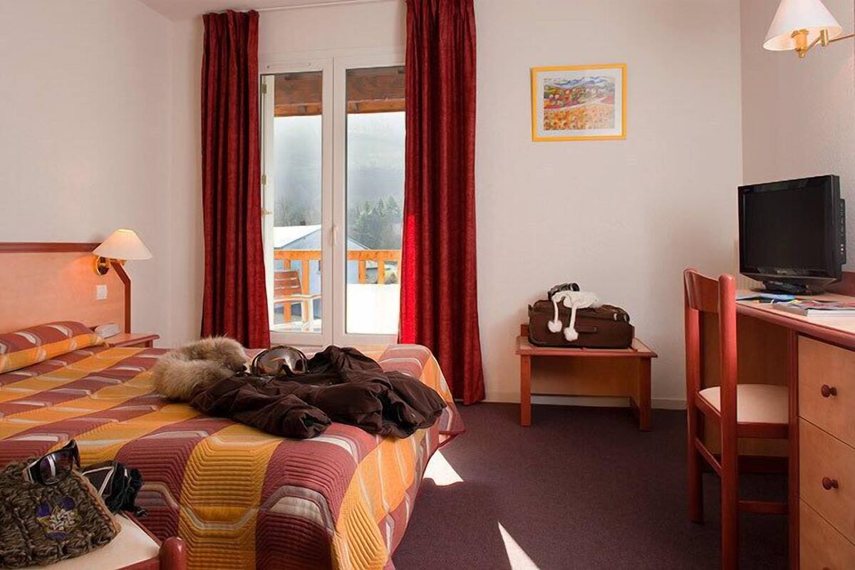 A hotel room with a bed, a desk, a television, and a window with curtains.