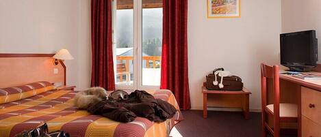 A hotel room with a bed, a desk, a television, and a window with curtains.