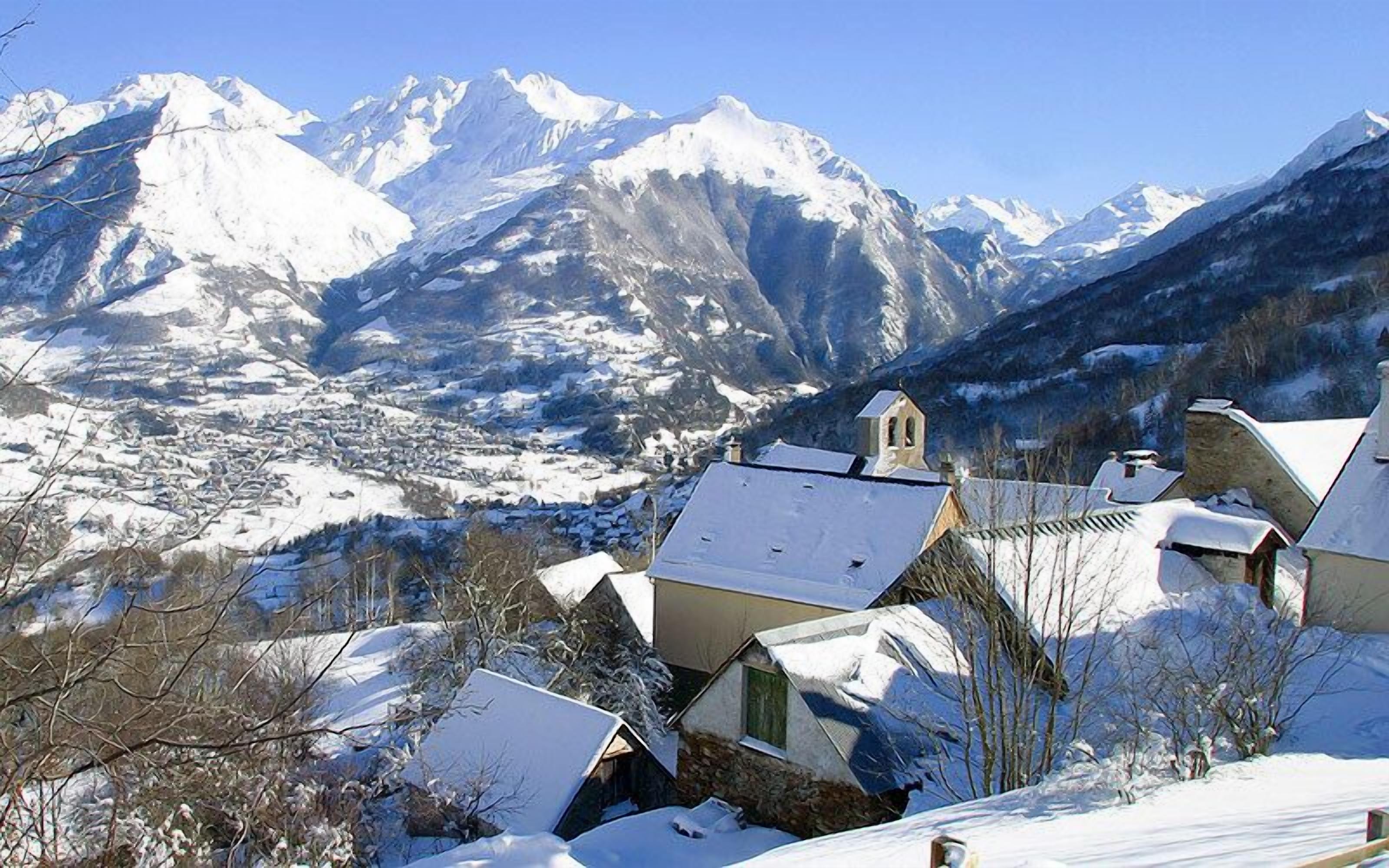 Un village enneigé, avec des bâtiments traditionnels et une chaîne de montagnes en arrière-plan.