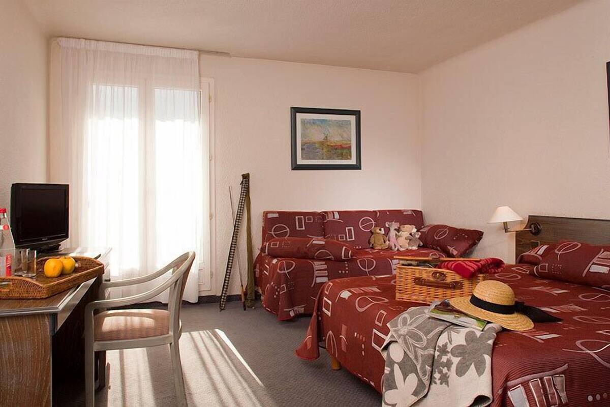 A hotel room with a desk, two beds, a television, and a painting on the wall.
