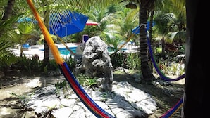 Uma rede, uma formação rochosa e uma piscina em um cenário tropical.