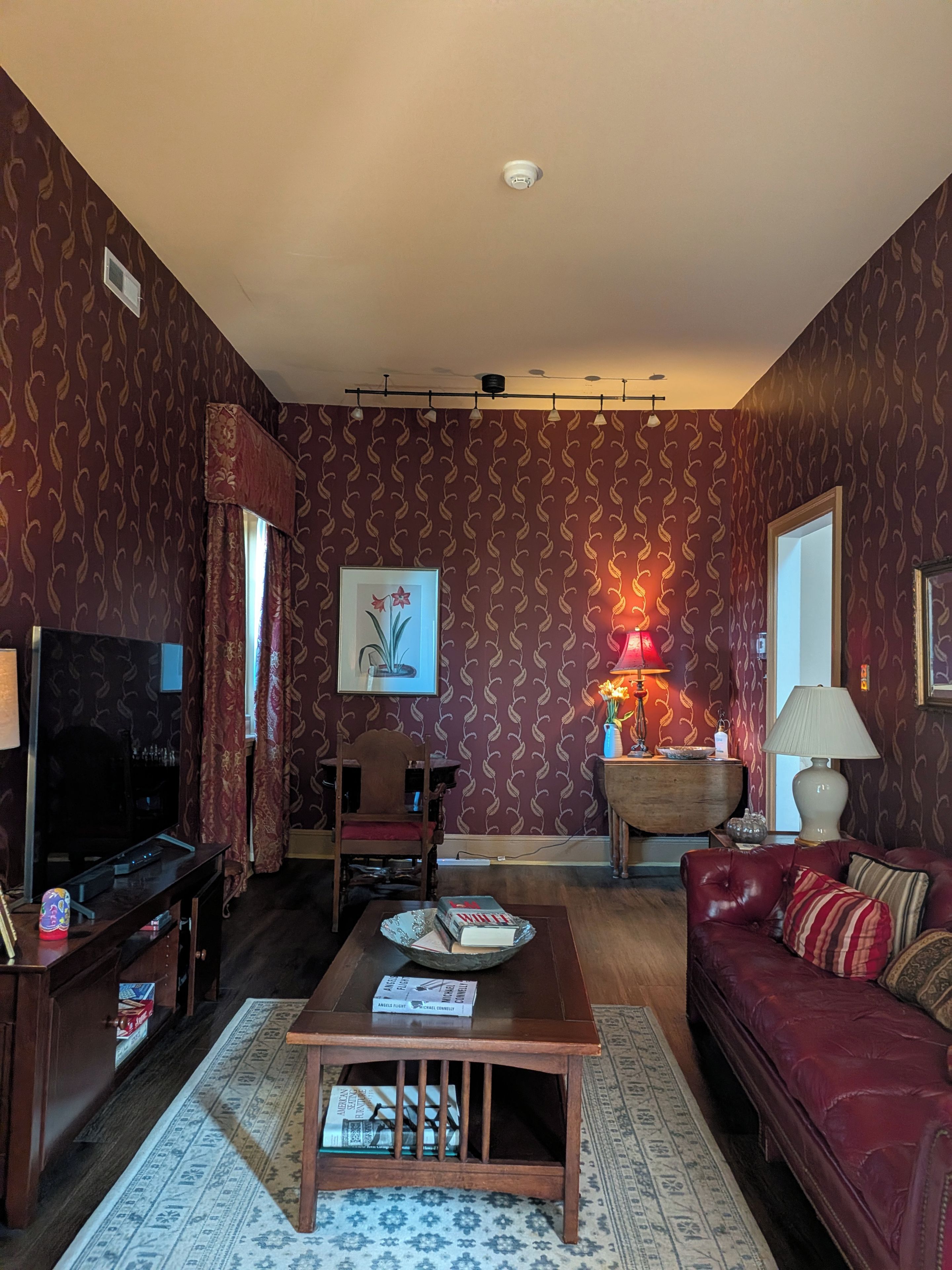 A living room with a television, sofa, table, and patterned wallpaper.