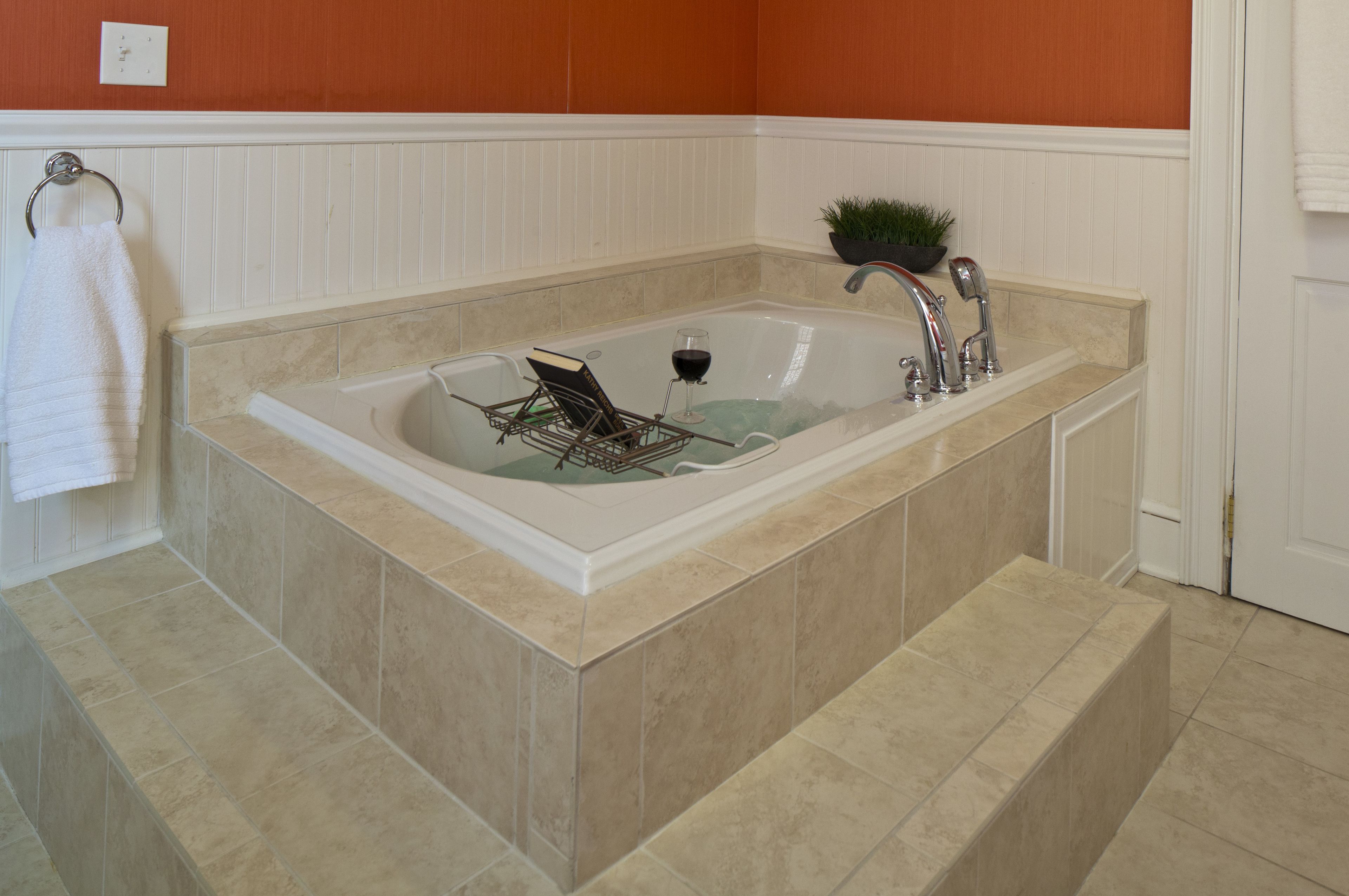 A large freestanding bathtub with a built-in seat and a small plant on the side.