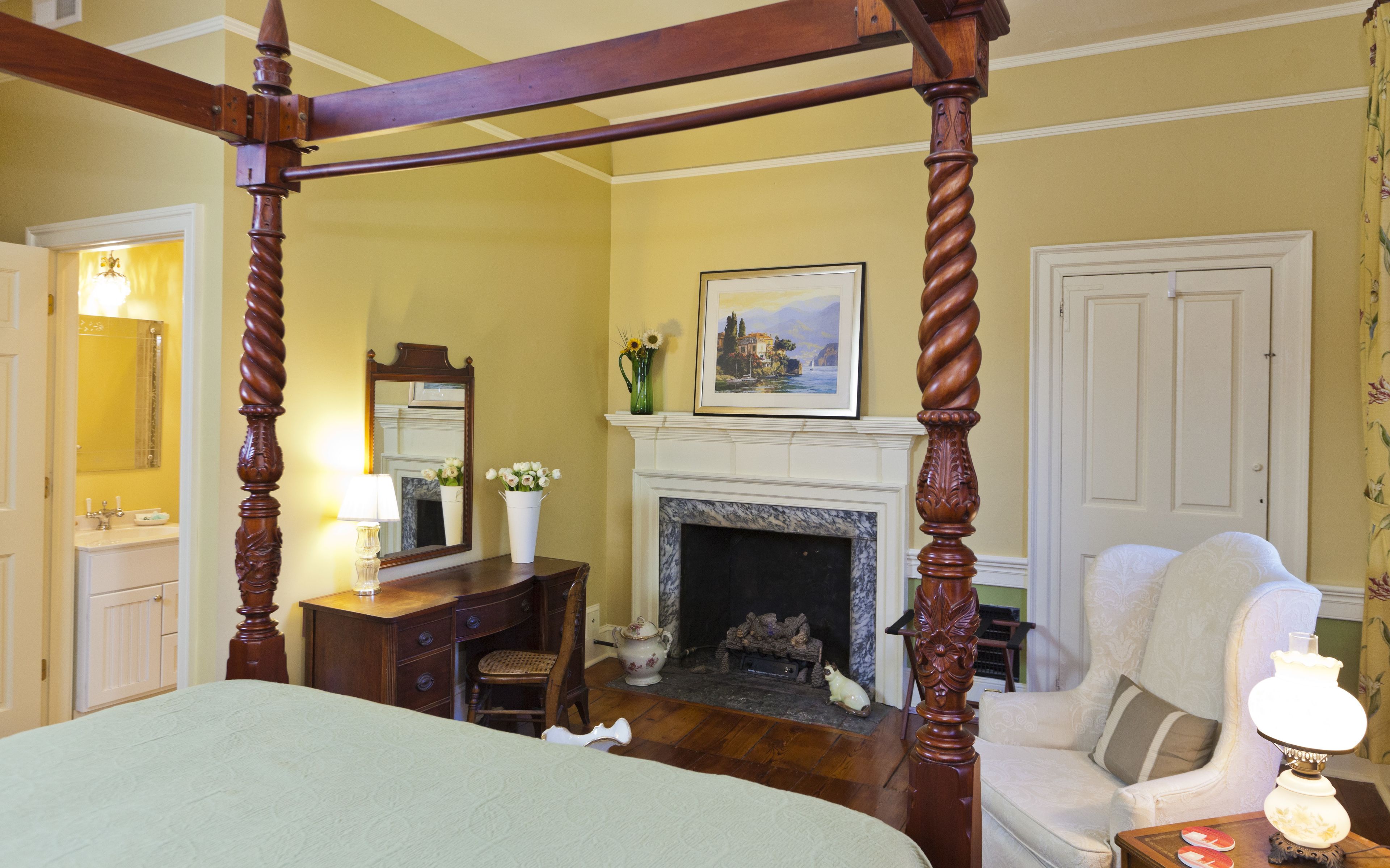 Un dormitorio tradicional con cama con dosel, chimenea, escritorio con lámpara y una silla.