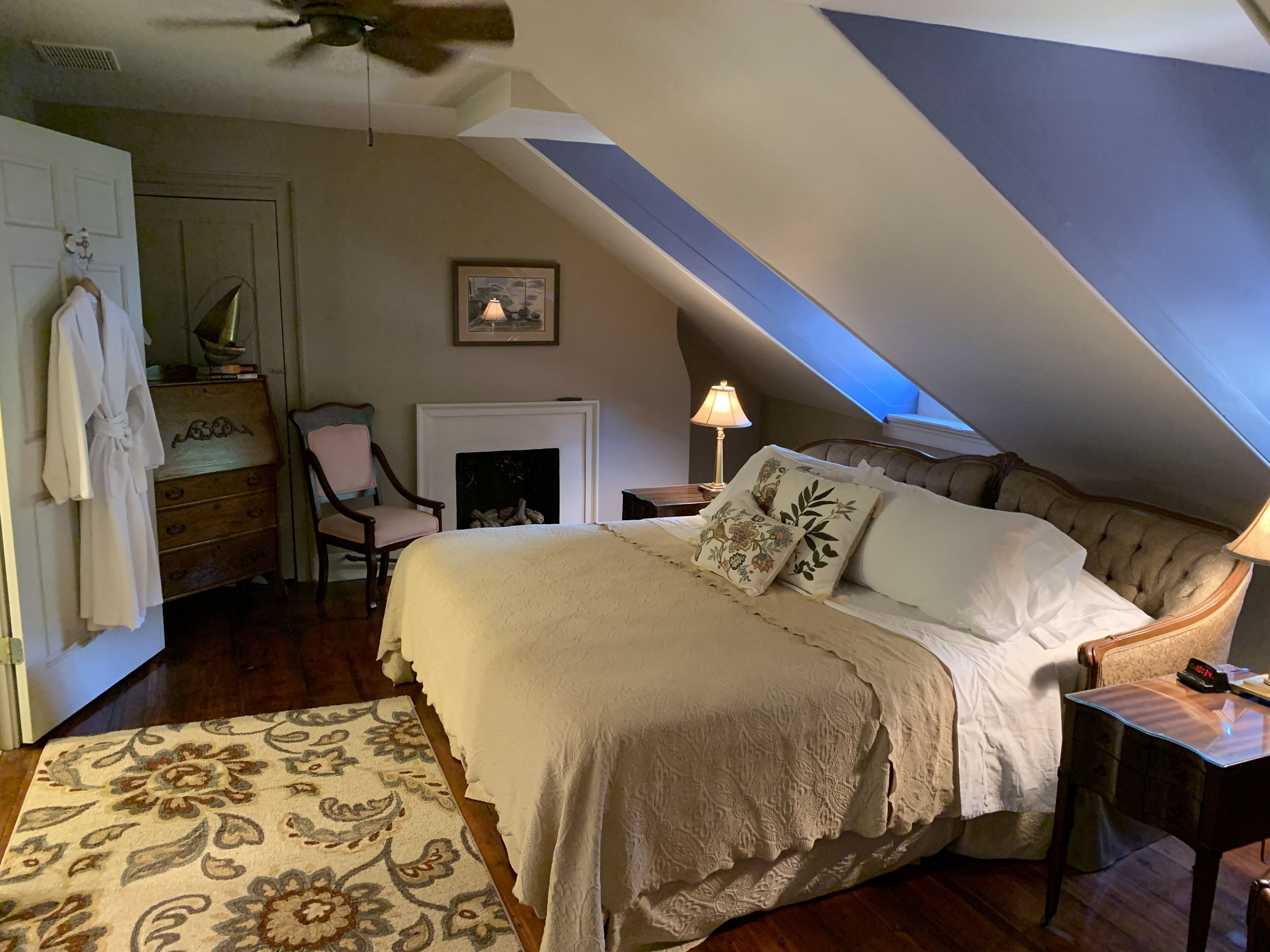 A bedroom with a large bed, a fireplace, a desk, and a chair.