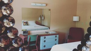 A hotel room with a bed, a desk, a chair, a mirror, and a lamp. - Holiday Music Motel (Sturgeon Bay)