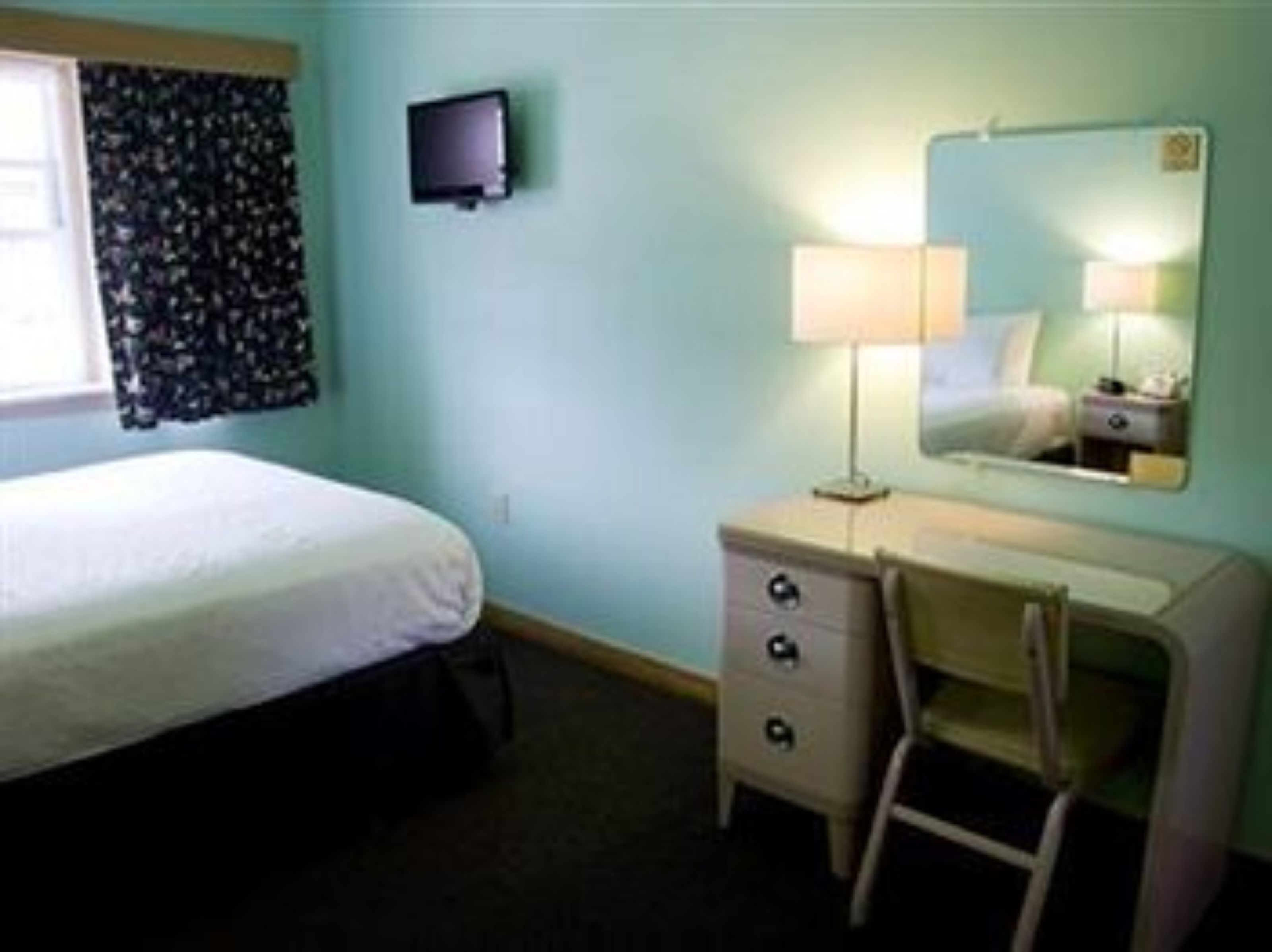 A hotel room with a bed, a desk with a chair, a television, and a mirror.