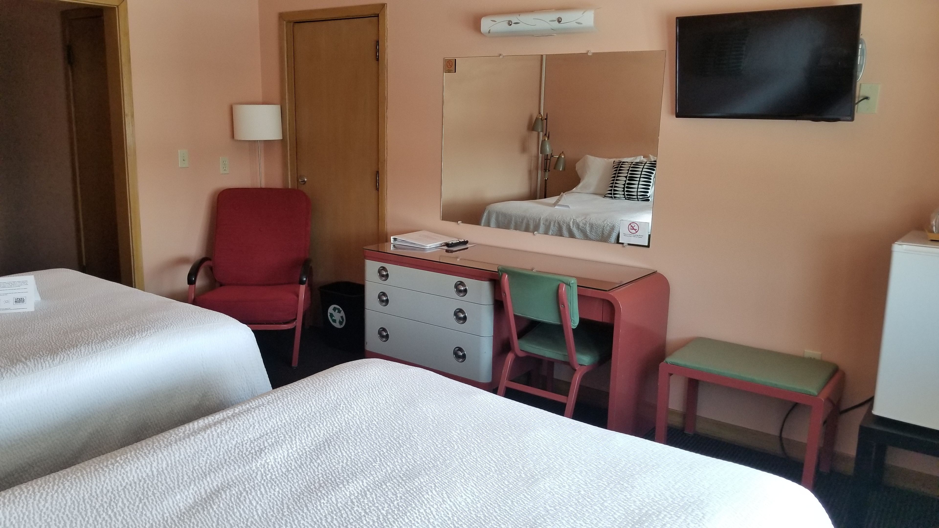 Ein Hotelzimmer mit zwei Betten, einem Schreibtisch, einem Stuhl, einem Schminktisch und einem Fernseher.