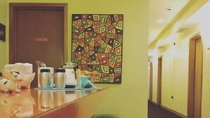 A hotel lobby with a long reception desk, green cushioned seating, a colorful abstract painting, and a door marked "EXIT". - Holiday Music Motel (Sturgeon Bay)