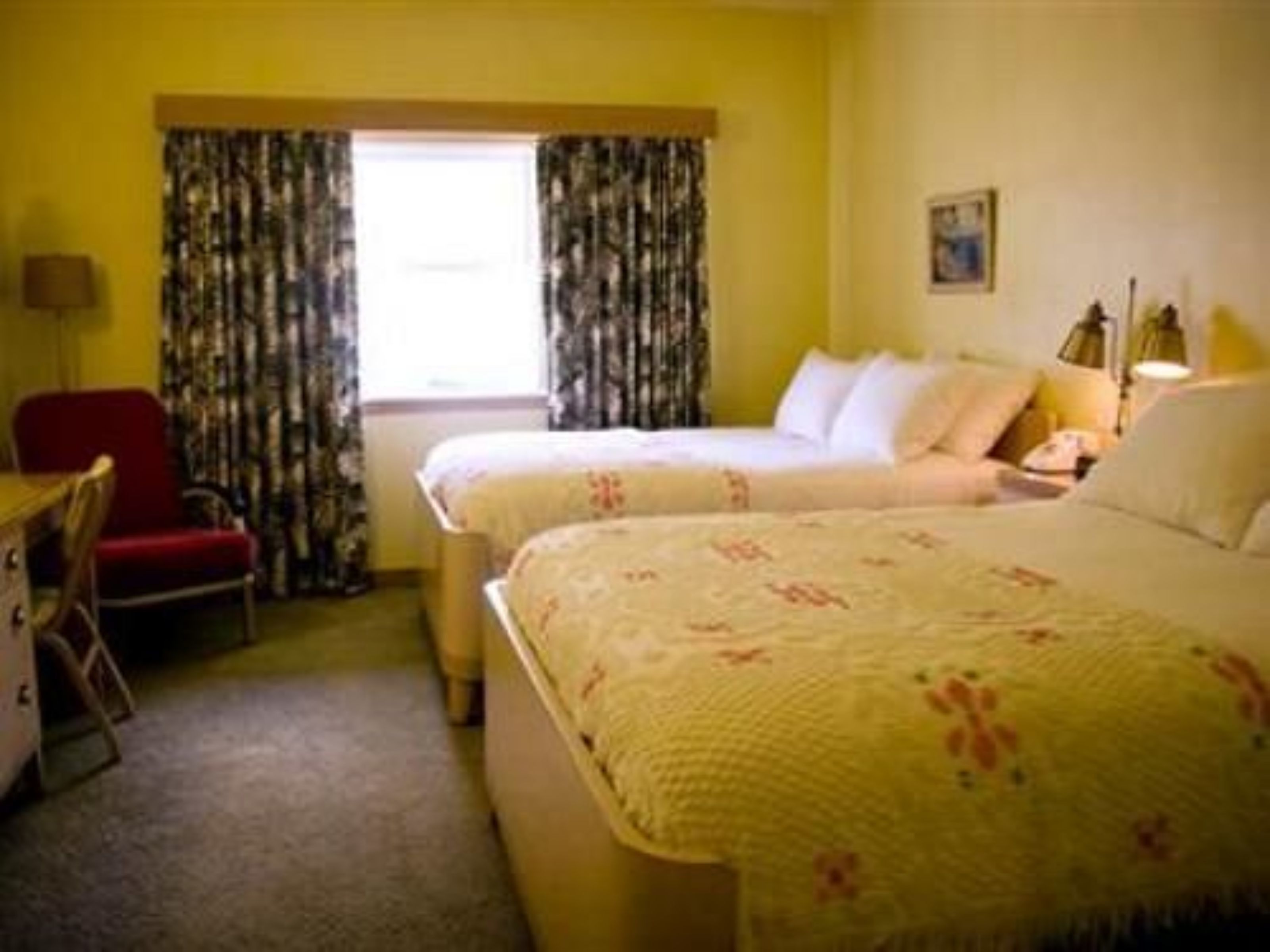 Habitación de hotel con dos camas, un escritorio, una silla y un ventanal con cortinas.