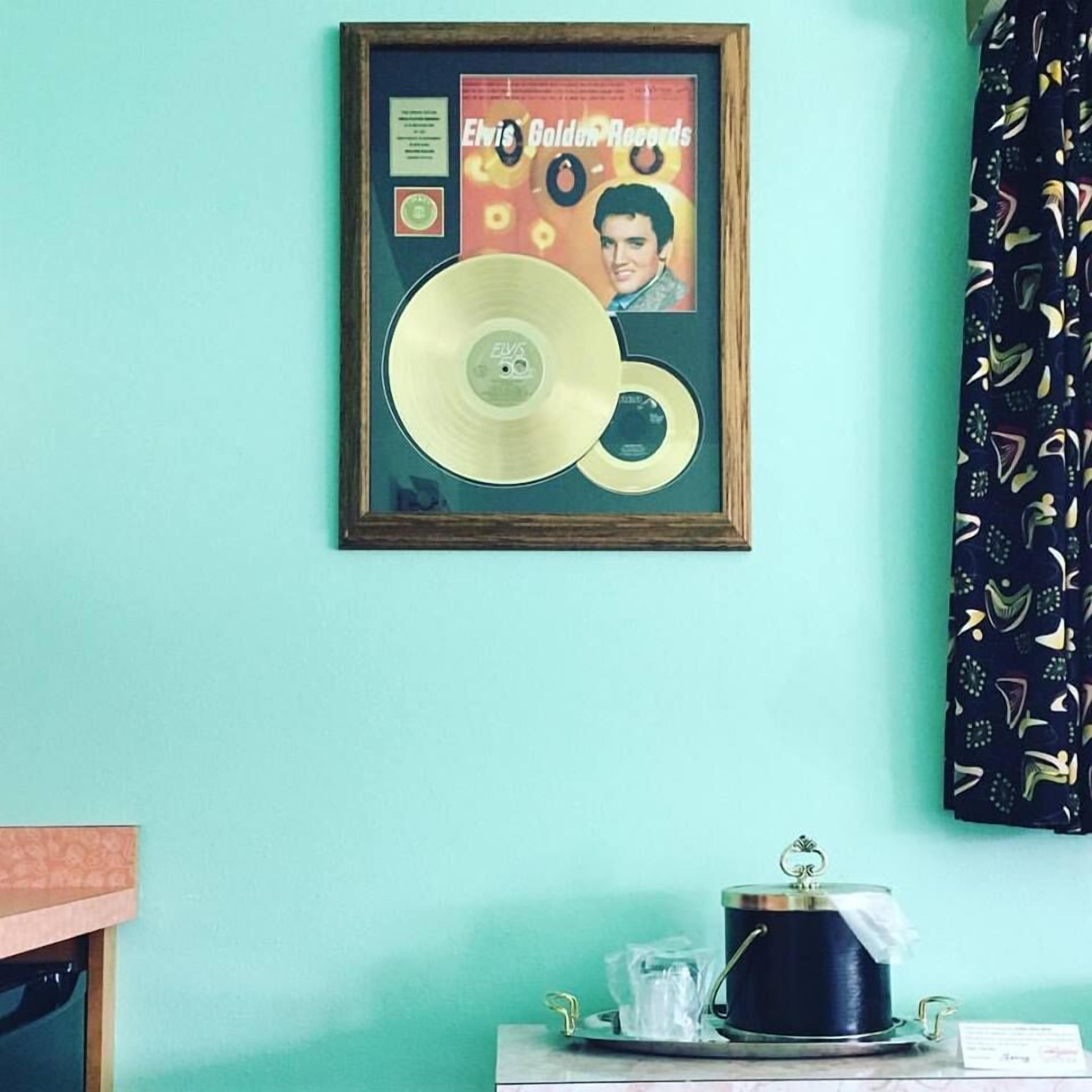 Une pochette d’album d’Elvis Presley, encadrée, est accrochée à un mur de couleur turquoise.