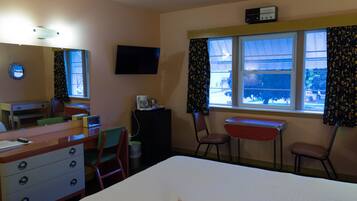 A hotel room with a bed, a desk, a chair, a dresser, a television, and a window with curtains.