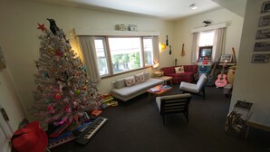 A cozy living room with a Christmas tree, a sofa, a coffee table, and a red armchair. There are guitars and a keyboard on the floor. - Holiday Music Motel (Sturgeon Bay)