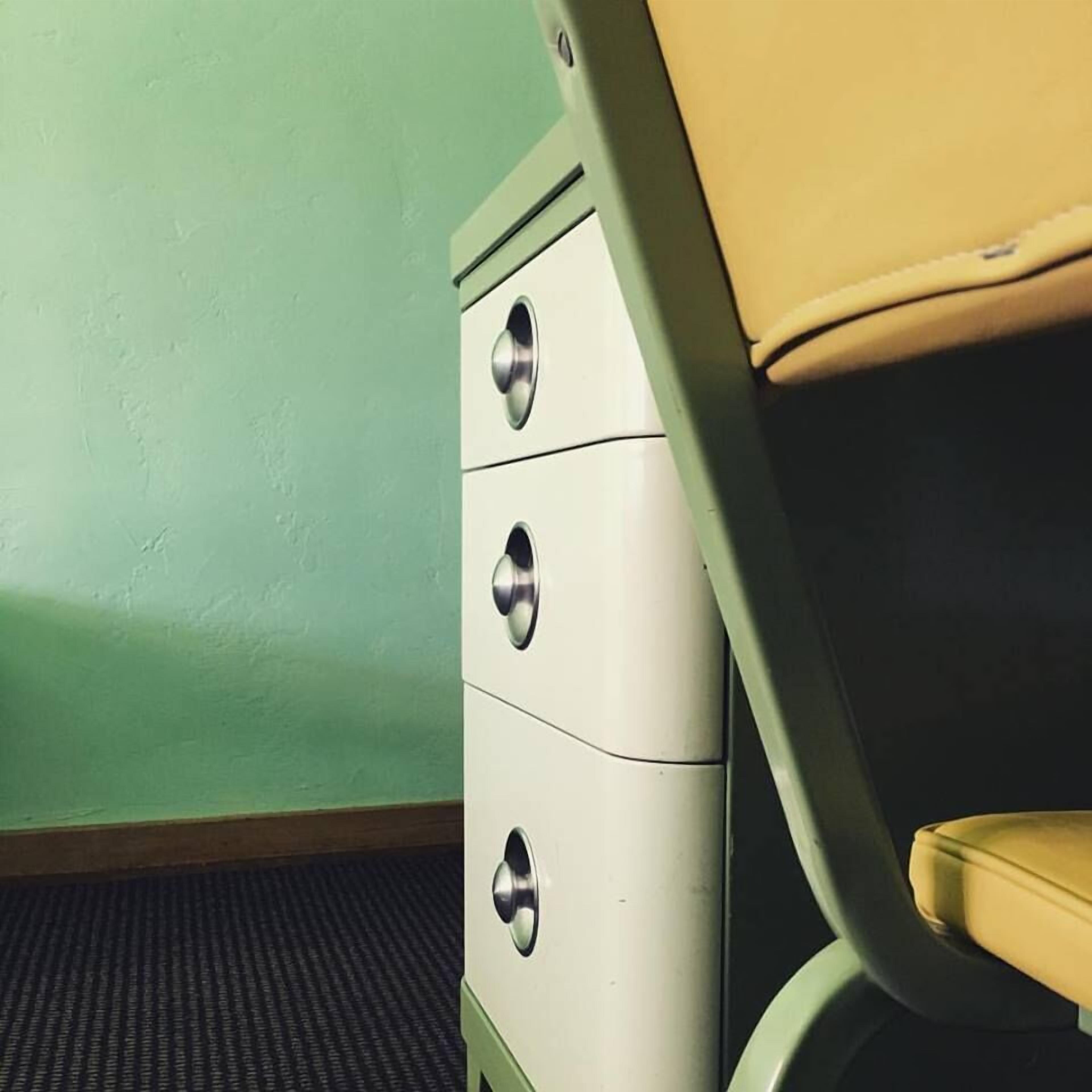 A room with a green wall, a white chest of drawers, and a yellow chair.