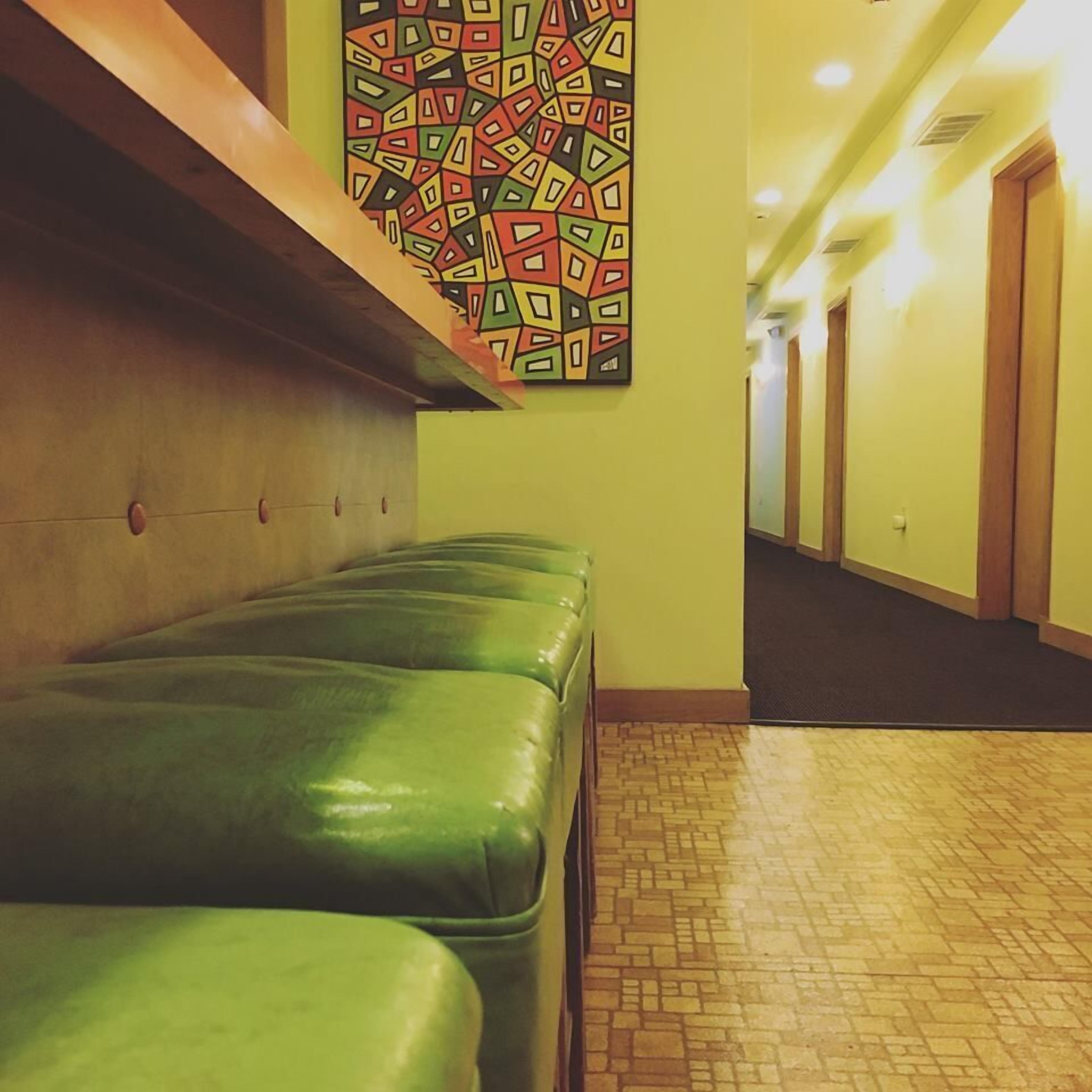 A hallway with green cushioned benches, a patterned wall art, and a tiled floor.