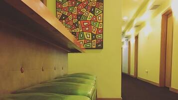 A hallway with green cushioned benches, a patterned wall art, and a tiled floor.