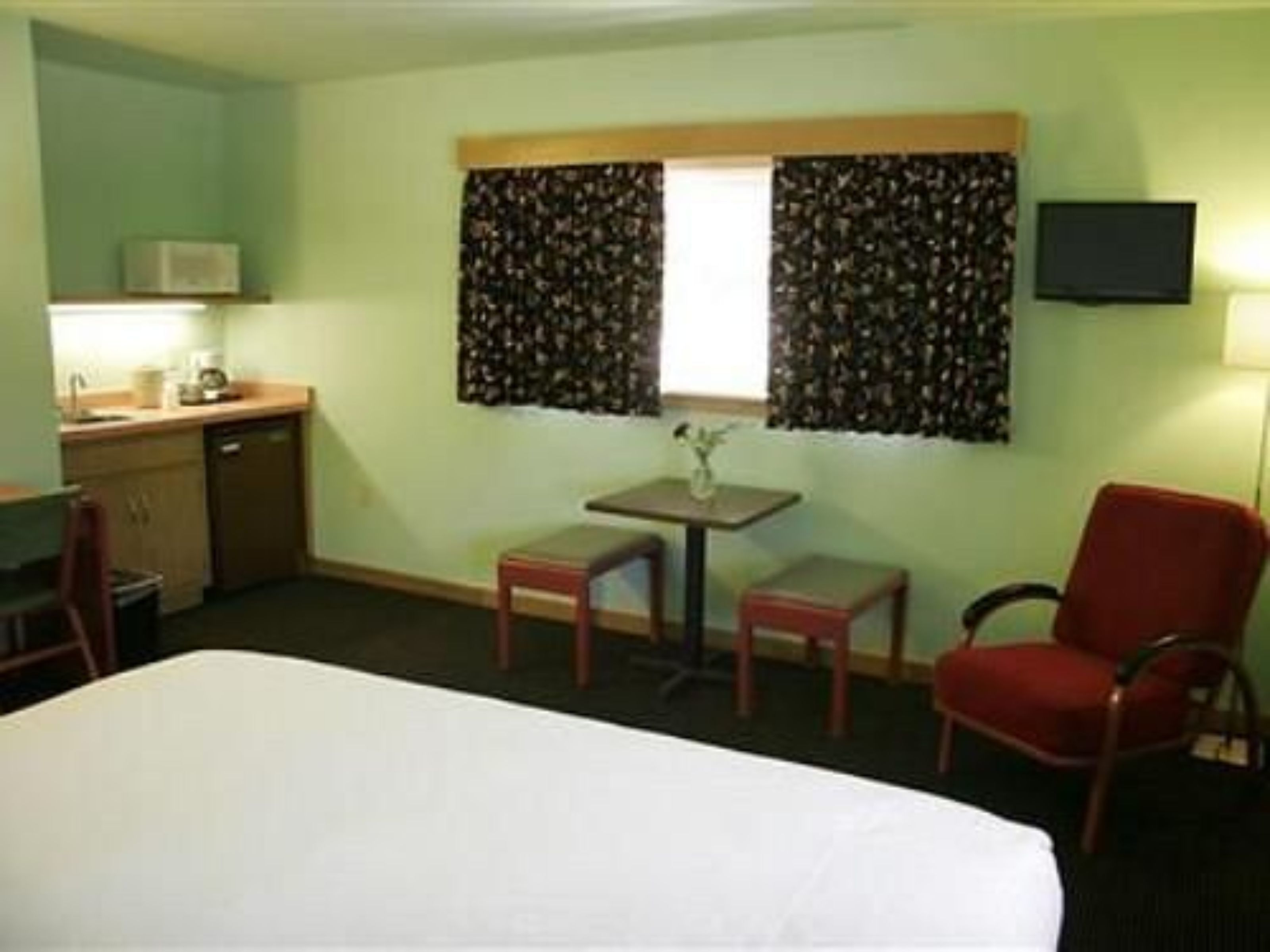 Une chambre d’hôtel avec un lit, une petite table sur laquelle est posé un vase, une chaise, un bureau avec une lampe et un téléviseur fixé au mur.