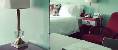 Una habitación de hotel con una cama, una mesita de noche con una lámpara, una silla roja y un escritorio con una lámpara y un libro.