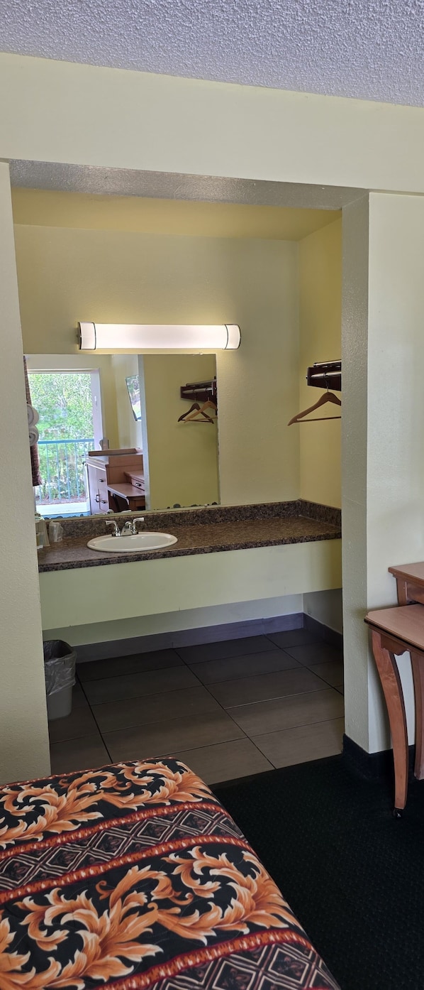 Une chambre d’hôtel avec un lit, une salle de bain comprenant un lavabo et un miroir, et une vue sur l’extérieur.