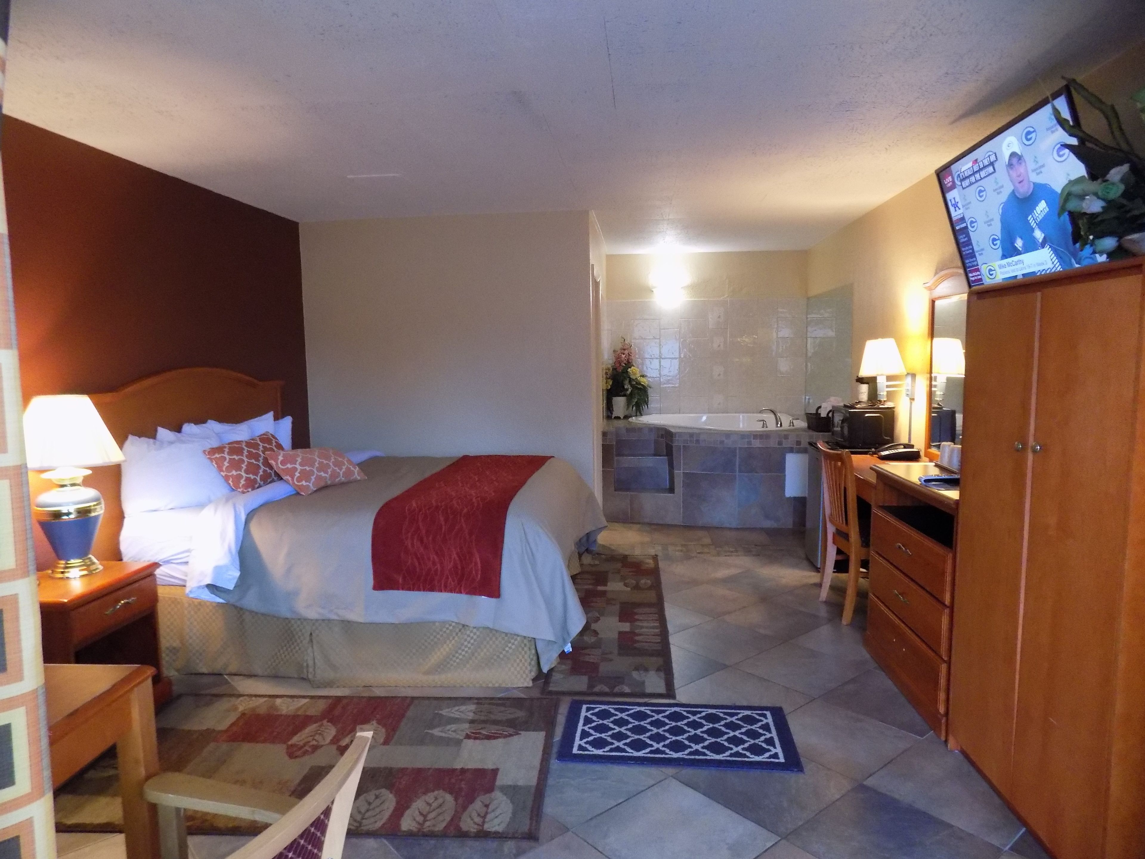 Ein Hotelzimmer mit Bett, Nachttisch, Lampe und einem Fernseher, der eine Nachrichtensendung zeigt.