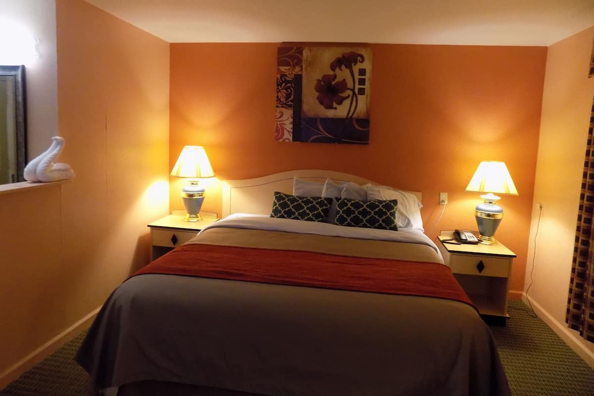 A hotel room with a bed, two bedside lamps, a painting on the wall, and a swan decoration on the window sill.