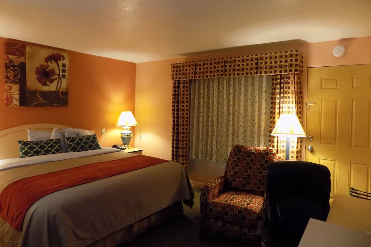 A hotel room with a bed, two bedside lamps, a chair, a curtain, and a door.