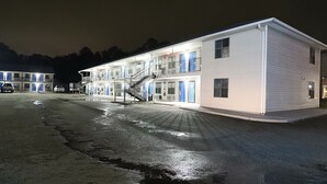 Un motel con una escalera central, varias habitaciones con puertas azules y un área de estacionamiento.