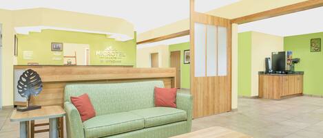 Un espace d’accueil d’hôtel avec un canapé vert, un comptoir de réception en bois et un téléviseur posé sur un meuble.