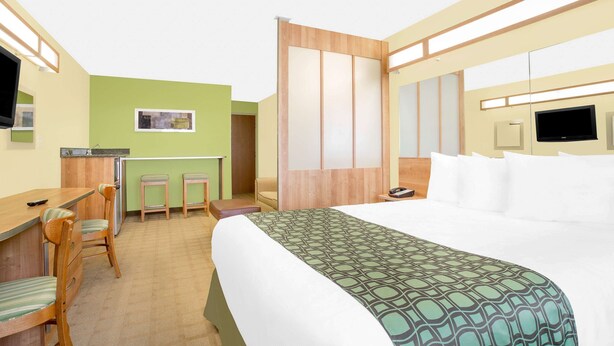A hotel room with a bed, a desk with chairs, a small kitchenette, and a TV.