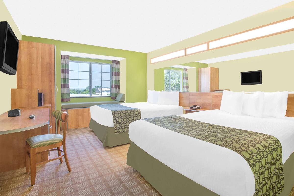 A hotel room with two beds, a desk, a chair, a TV, and a window with curtains.