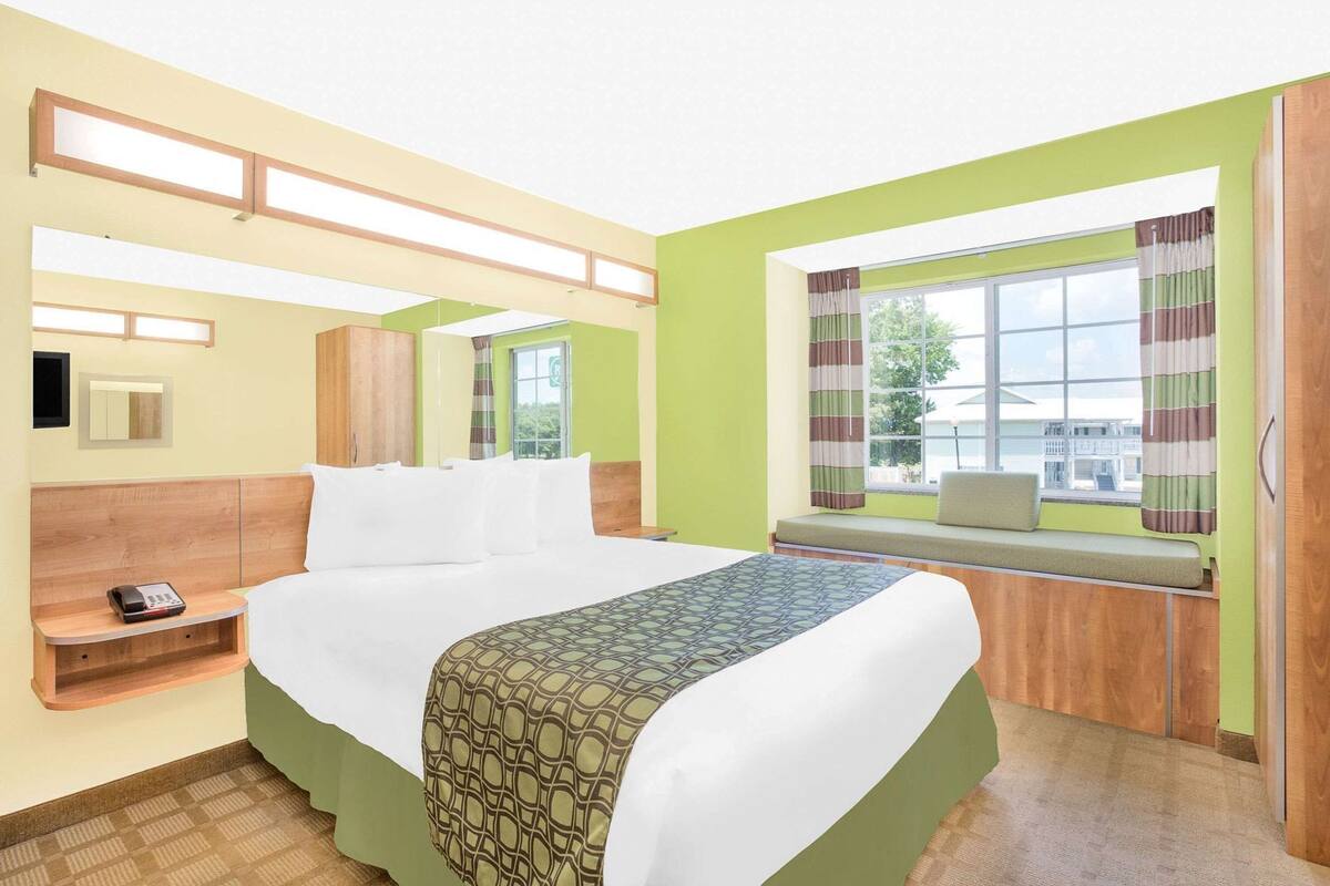 A hotel room with a bed, bedside table, and a window with curtains.