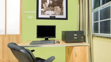 Un espace de travail comprenant un ordinateur, un clavier, une souris et un fauteuil de bureau. Un cadre avec une photographie est accroché au mur, et il y a une fenêtre avec des rideaux.