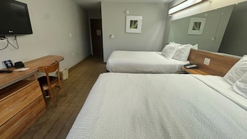 Hotellihuone, jossa on kaksi sänkyä, työpöytä, tuoli, televisio ja peili.