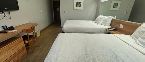 A hotel room with two beds, a desk, a chair, a television, and a mirror.