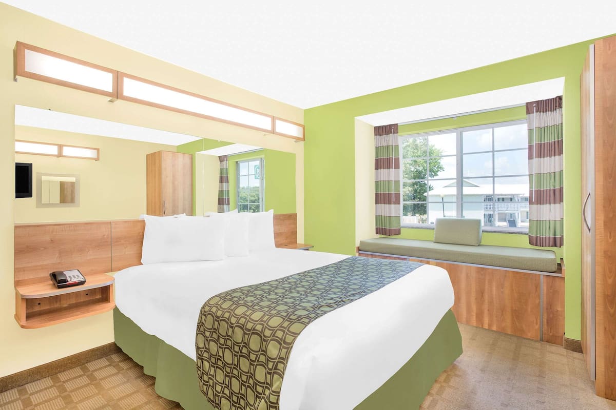 A hotel room with a large bed, a bedside table with a phone, a window with curtains, and a view of the outside.