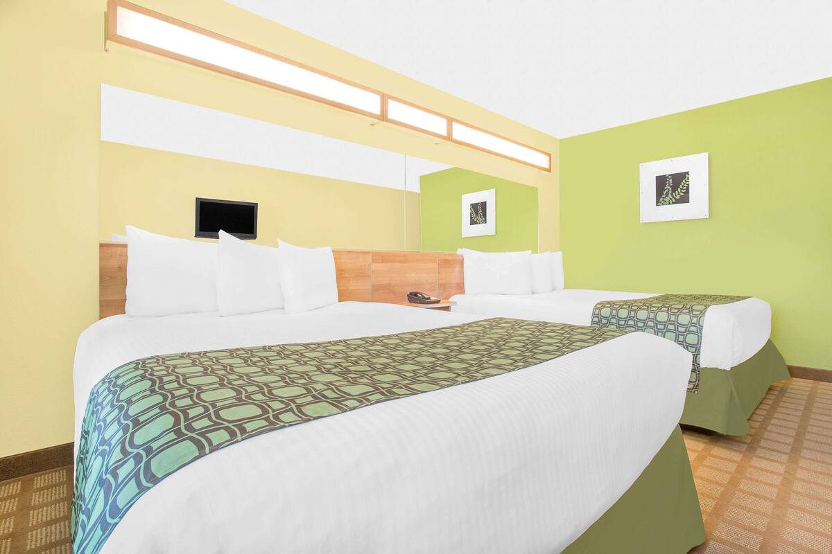 A hotel room with two beds, a wooden headboard, a flat-screen TV, and artwork on the walls.