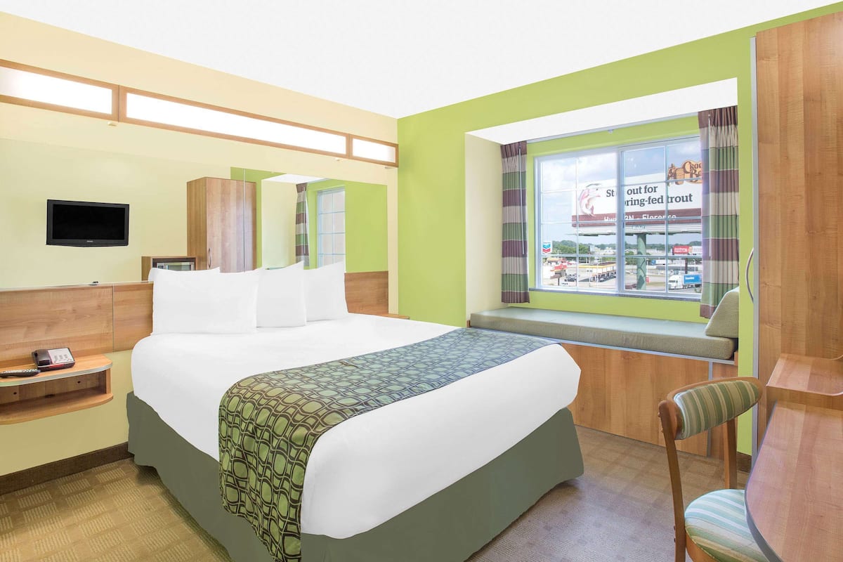 A hotel room with a bed, a TV, a window with a view of a store, and a desk with a chair.