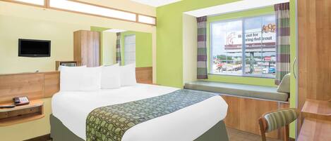A hotel room with a bed, a TV, a window with a view of a store, and a desk with a chair.