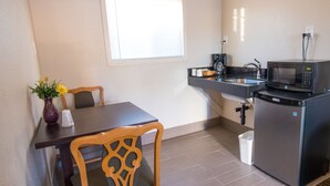 A compact kitchen with a microwave, sink, and a small refrigerator. There is a dining table with chairs and a vase with flowers. - Budget Lodge Eugene (Eugene)