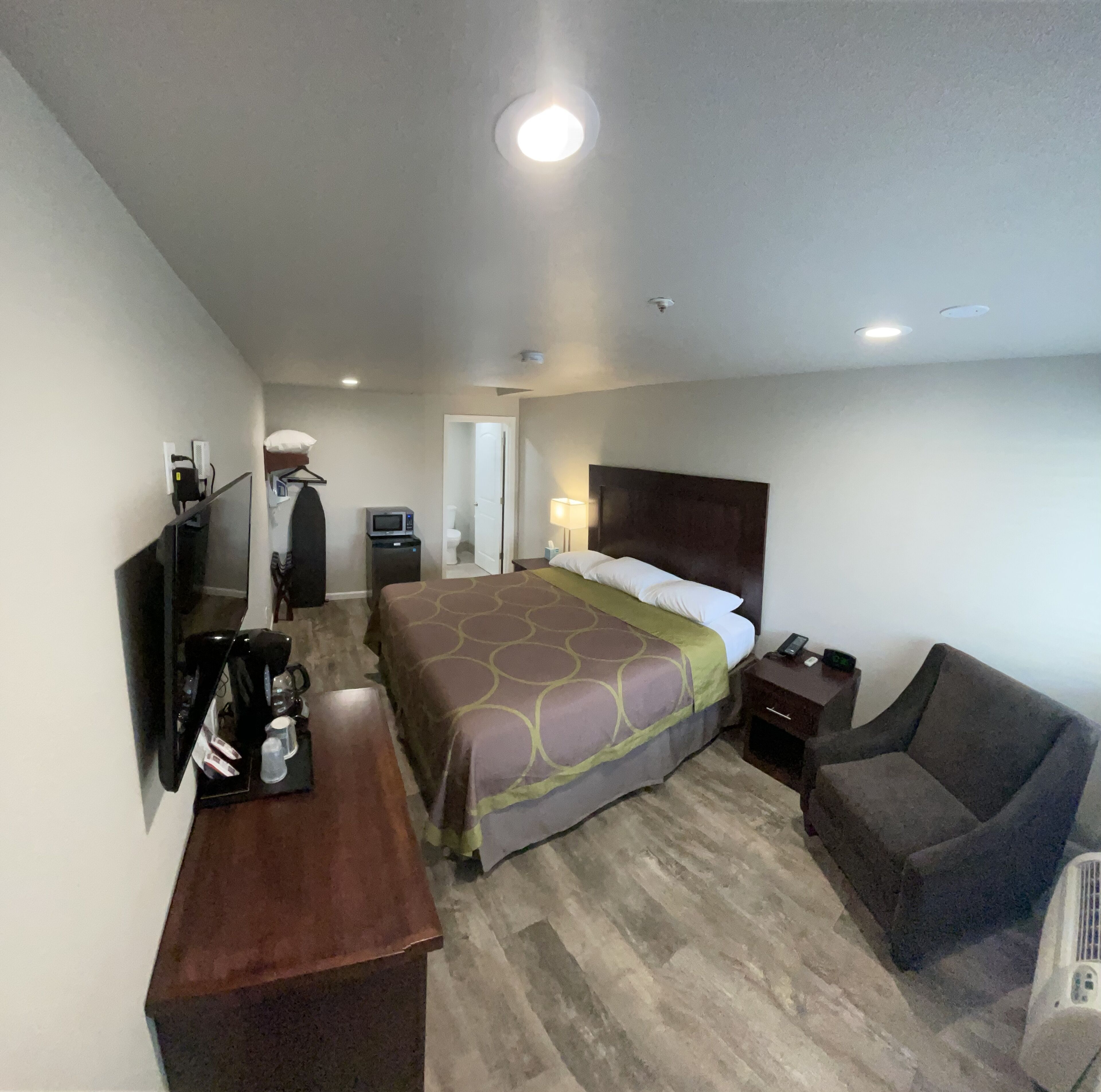 A hotel room with a bed, a desk, a chair, a TV, and a small table with a coffee maker.