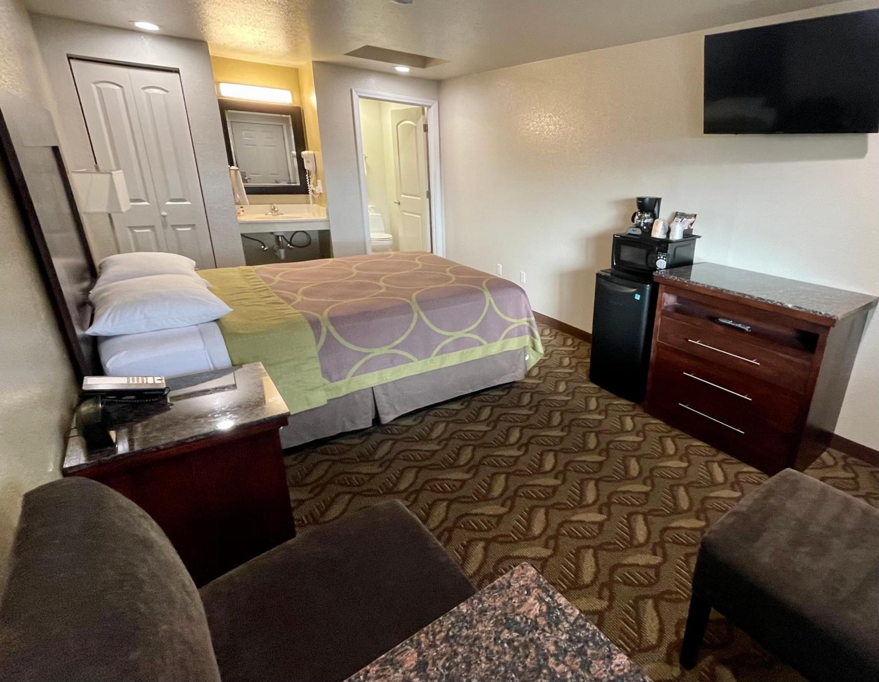A hotel room with a bed, a desk with a telephone, a microwave, a TV, and a dresser.